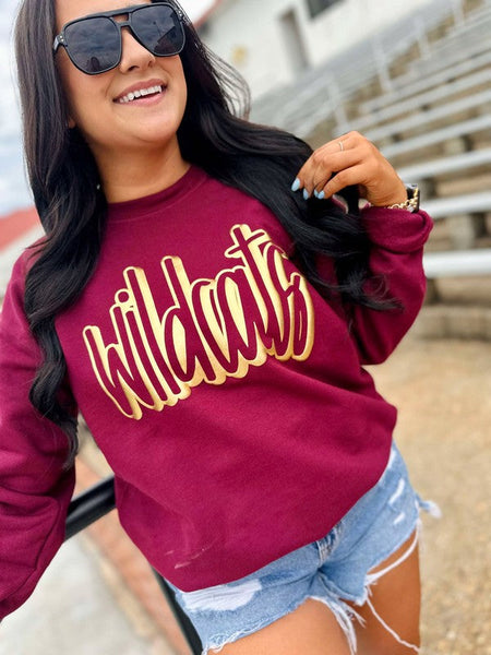 Woman wearing a maroon sweatshirt with 'Wildcats' in gold letters and denim shorts.