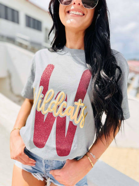 Woman wearing a gray t-shirt with 'Wildcats' printed on it, standing outdoors.
