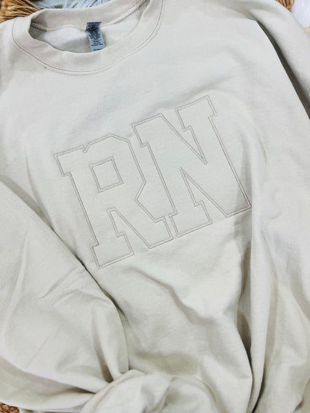 A beige embroidered sweatshirt with the letters 'RN' on the front.