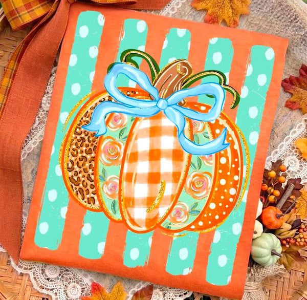 A square fabric tote bag with an autumn-themed design, featuring three stylized pumpkins with leopard print, orange-and-white gingham, and orange-and-white polka dot patterns, decorated with a light blue ribbon bow. The bag has a bright orange border with white polka dots and is displayed on a decorative autumn-themed surface with lace, fall leaves, and small pumpkins.