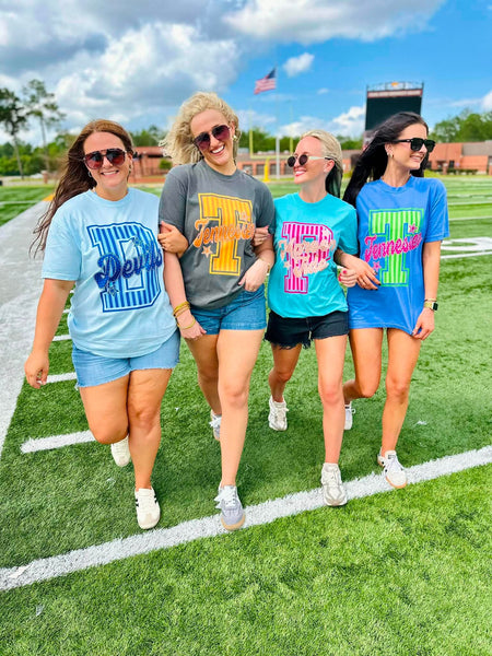 Four women walking on a football field wearing matching t-shirts with different designs.